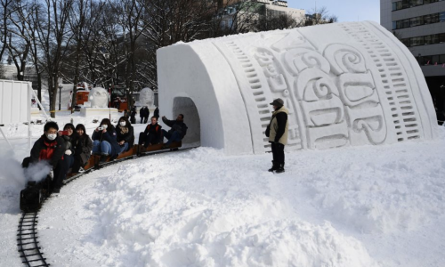 Photograph of festival goers riding a miniature railroad through a Cup of Noodle snow sculpture at the 2020 Sapporo Snow Festival (from Jozuka, 2020).