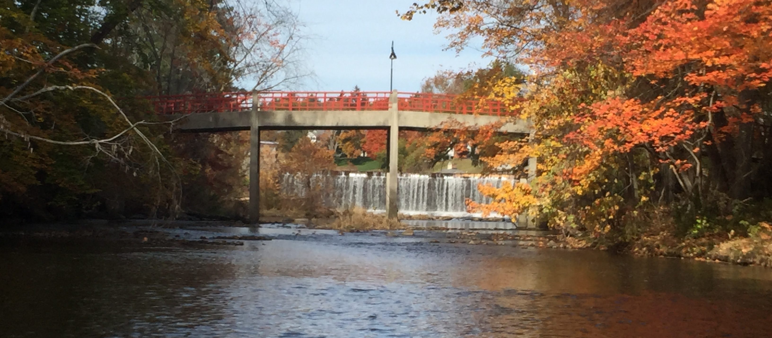 image of the Mill River looking upstream at Lamont Bridge and the spillway from Paradise Pond on the Smith College campus in the fall with orange, yellow, and green leaves. 