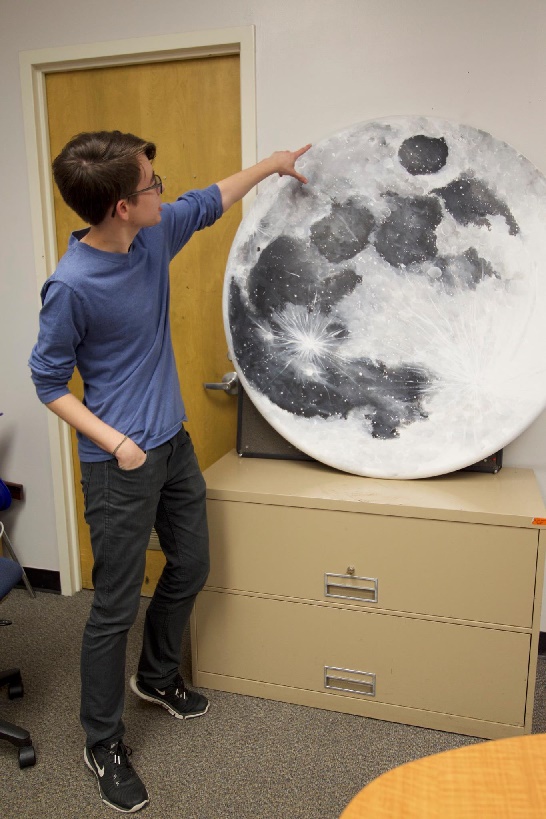Eliot Halley pointing to a very large painting of the Moon